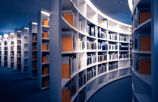 Hallway perspective of a line of white bookshelves filled with books and orange partitions; photo credit: Martin Adams / Unsplash