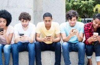 a group of teens sitting and on their phones outside