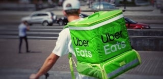 Behind view of a bike-delivery man who has an Uber Eats insulated delivery box on his back. Photo credit for Robert Anasch, Unsplash.