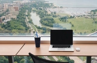 Laptop on desk next to window overlooking city, Photo Credit: Tanner Van Dera / Unsplash