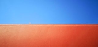 Lower-angle image of an orange wall in the bottom half and a clear blue sky in the top half. Photo by Jac Alexandru for Unsplash.