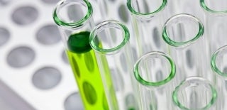 Test tube tray partially filled with empty test tubes. The left most test tube is filled with a clear, light green liquid. Photo by Bill Oxford on Unsplash.