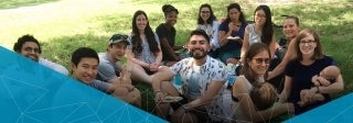 Large group of people sitting on the grass and smiling at the camera