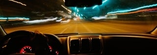 View from inside a car at night, looking out at the road ahead. A long exposure has created colorful trails from the lights