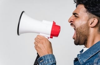 man wearing a denim jacket shouting into red and white megaphone. photo credit Sora Shimazaki/Pexels