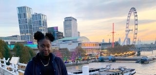 Khristina Spence in front of the Thames River with the London Eye and various buildings behind her