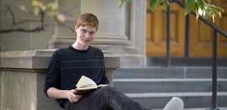 Student seated outside a building with a book in their lap