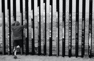 person looking through fence at US-Mexico border; Photo by Max Bohme on Unsplash