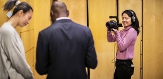 a student holding a video camera shoots footage of two other people