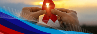 Hands holding up a red HIV ribbon in front of a sunset