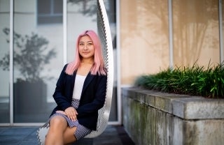 Woman with pink hair sitting on a bench outdoors and looking at the camera