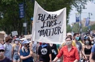 Protestors wearing COVID-protective facemasks march holding Black Lives Matter signs
