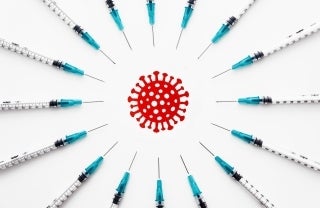 Syringes arranged in a circle around a red graphic illustration of coronavirus