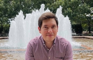 Juan Llamas Rodriguez 1920 x 1250.jpg Juan Llamas-Rodriguez smiling outdoors in front of a fountain and trees behind the fountain