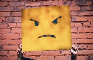 Two hands holding up a sign with an angry face illustration