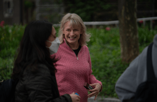 Diana Mutz wearing a pink sweater and smiling at a passing student outside
