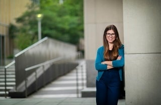 Ava Kikut smiling with her arms crossed and leaning against an exterior wall of the Annenberg School building