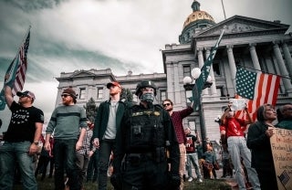 Protesters holding flags and protest signs in front of the Colorado state Capitol with a member of the police or military in riot gear. Credit: Chris Lloyd / Unsplash