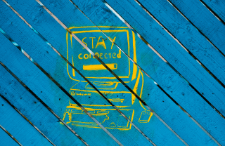 Yellow graffiti on blue wood slats of desktop computer with the words "Stay Connected" written on the monitor