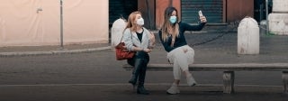 two women recording themselves on a phone while wearing face masks. Gabriella Clare Marino on Unsplash.