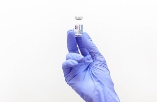 Gloved hand holding black and white labeled vaccine bottle