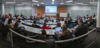 Fisheyed panorama of an event where many people sit in rows of tables, looking at someone at a podium. There is a screen in the front of the room.