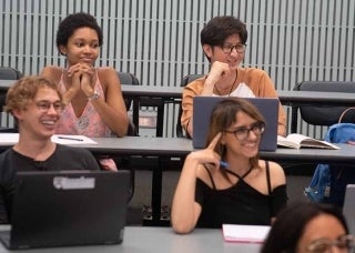 Students in a classroom listening and smiling to a speaker out of view