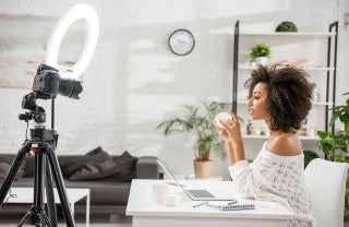 Side view of woman in modern looking room in front of camera and ring light filming a video.