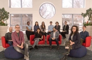 Professors and a group of 10 graduate students seated in a semi circle in the Plaza Lobby of the Annenberg School