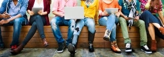 Seven young adults sitting on a bench and looking at their digital devices
