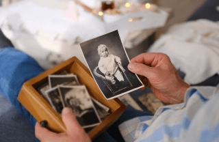 A closeup photo of a person holding a box of old photographs. In one hand, the person is holding a black and white photograph of a child