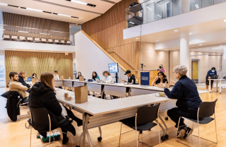 Students sit in black chairs around a large white conference table. Kathleen Hall Jamieson sits at the head of the table and is speaking