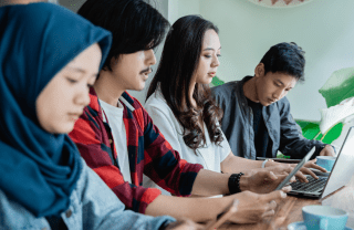 Four people sit next to one another at a cafe table looking down at their digital devices