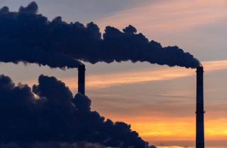 A sunset blocked by industrial chimneys blowing large plumes of smoke