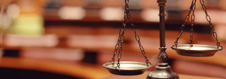 A bronze scale of justice sits in the foreground with a blurry background of books