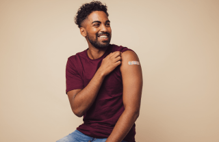 Man smiling after receiving vaccination - lifting up his sleeve to show bandage