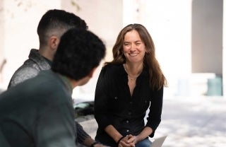 Emily Falk seated outside smiling at two people whose faces are unseen