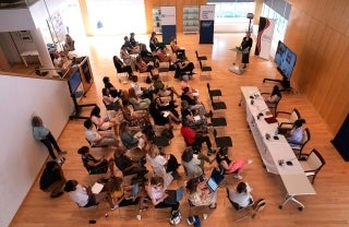 Wide view of The Agora showing many people seated in chairs and a speaker at a podium