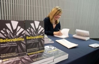 Sarah Banet-Weiser signing a book with copies of her book, Believability, in the foreground