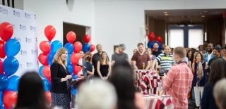 Sarah Banet-Weiser speaking at a podium with an audience and balloons around her