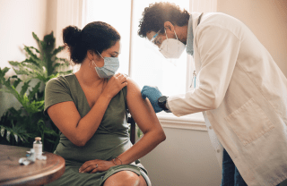 Woman in a blue mask receiving a COVID-19 vaccination from a doctor in a white mask