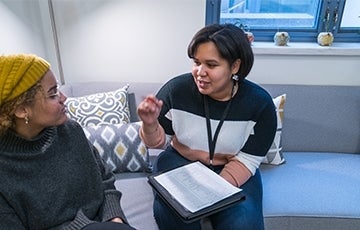 Alta and Jenna in 200 A woman with a clipboard, seated on a couch, speaks to another woman