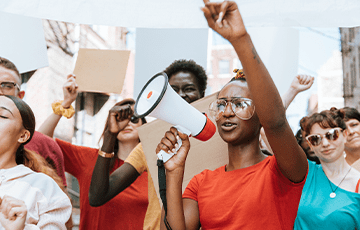Woman in orange shirt at a protest with megaphone, Photo Credit: Rawpixel on iStock