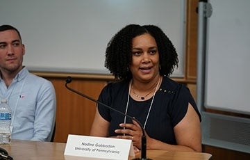 alumni 360 x 230.jpg A man and a woman seated at a table. The woman has a mic and is speaking