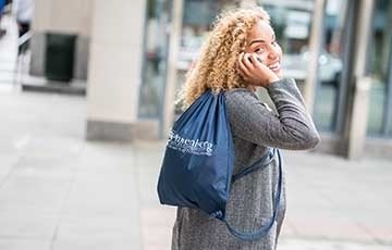 Jenna with Annenberg backpack 360 x 230.jpg Woman wearing Annenberg backpack on phone, looking behind her at the camera