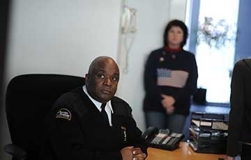 Ralph at desk 360 x 230.jpg Security guard seated at desk. Woman is blurred standing in the background.