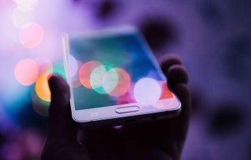 Photo of some holding a cellular device and dazzling lights around it. Photo credit: Rodion Kutsaev / Unsplash