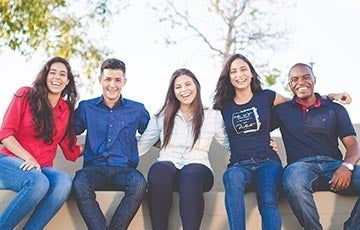 Five young people with arms around each other smiling for the camera . Photo credit Unsplash / Naassom Azevedo.