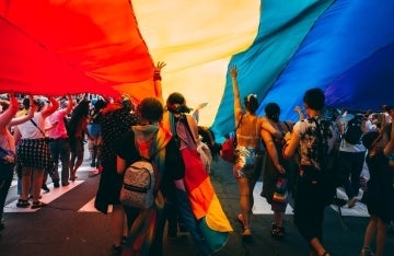 A photo of people under an LGBTQ flag at a Pride parade