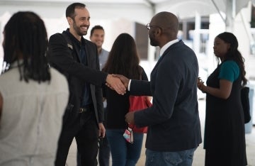 Two people shaking hands and others mingling under a large outdoor tent at the 2021 Professional Development Day